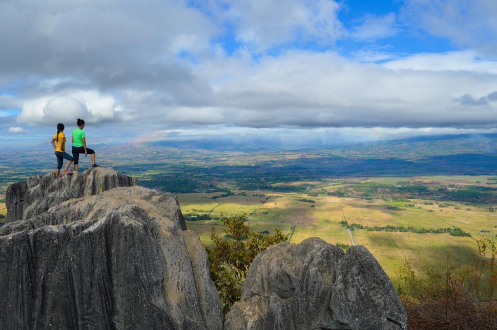 Free Image of Two hikers on rocky vantage point overlooking vast valley 