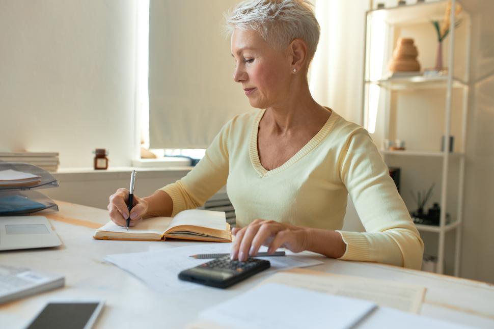 Free Image of Successful mature businesswoman working in her office, sitting at desk with papers and calculator, making notes, analyzing expenses. People, business, finances, planning and budget concept 