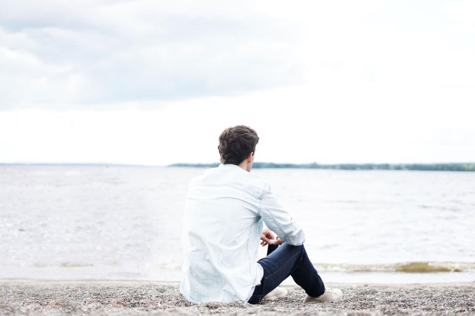 Free Image of Man sitting alone by the shore looking at the water 