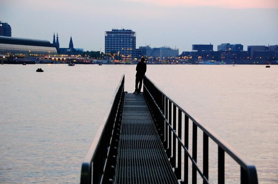 Free Image of Solitary figure on pier overlooking city waterfront at dusk 