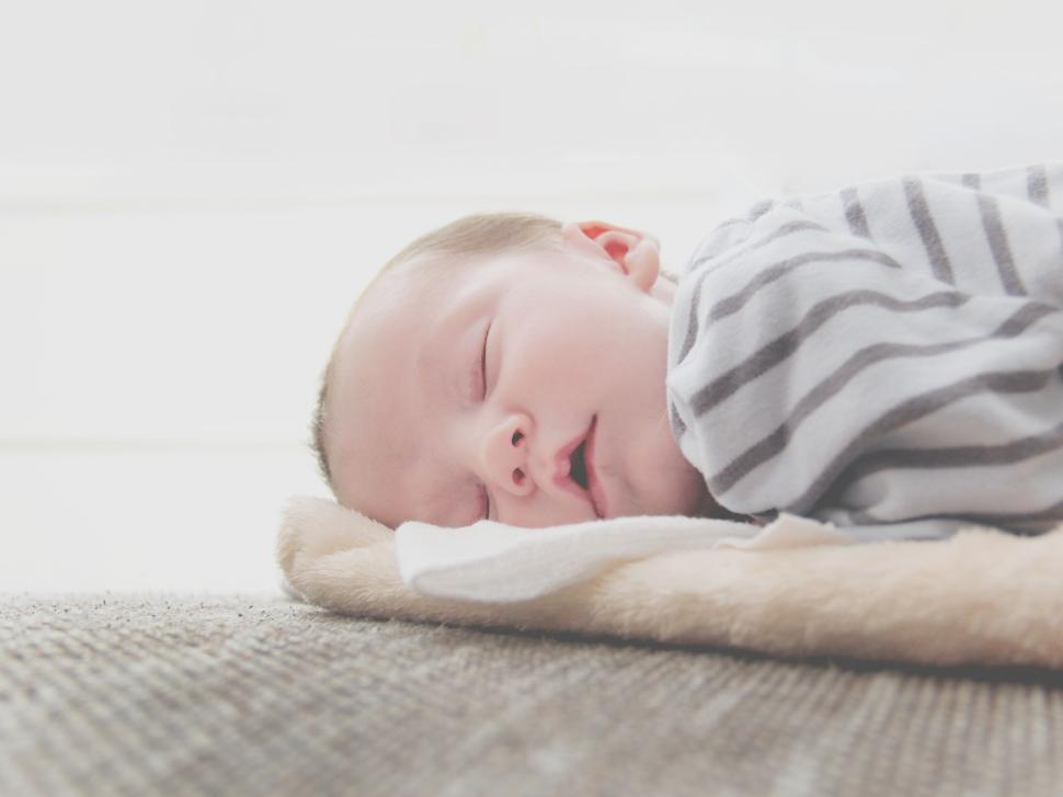 Free Image of Baby lying on blanket with striped outfit on floor. 