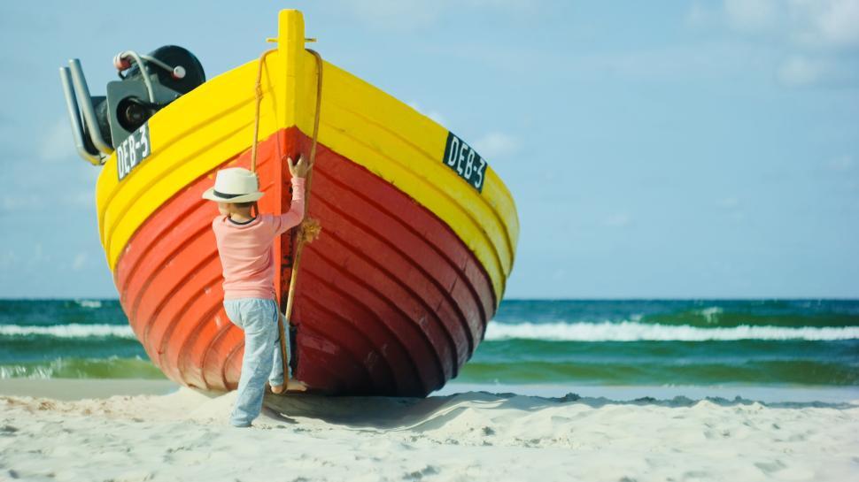Free Image of Colorful boat on sandy beach with person in hat 
