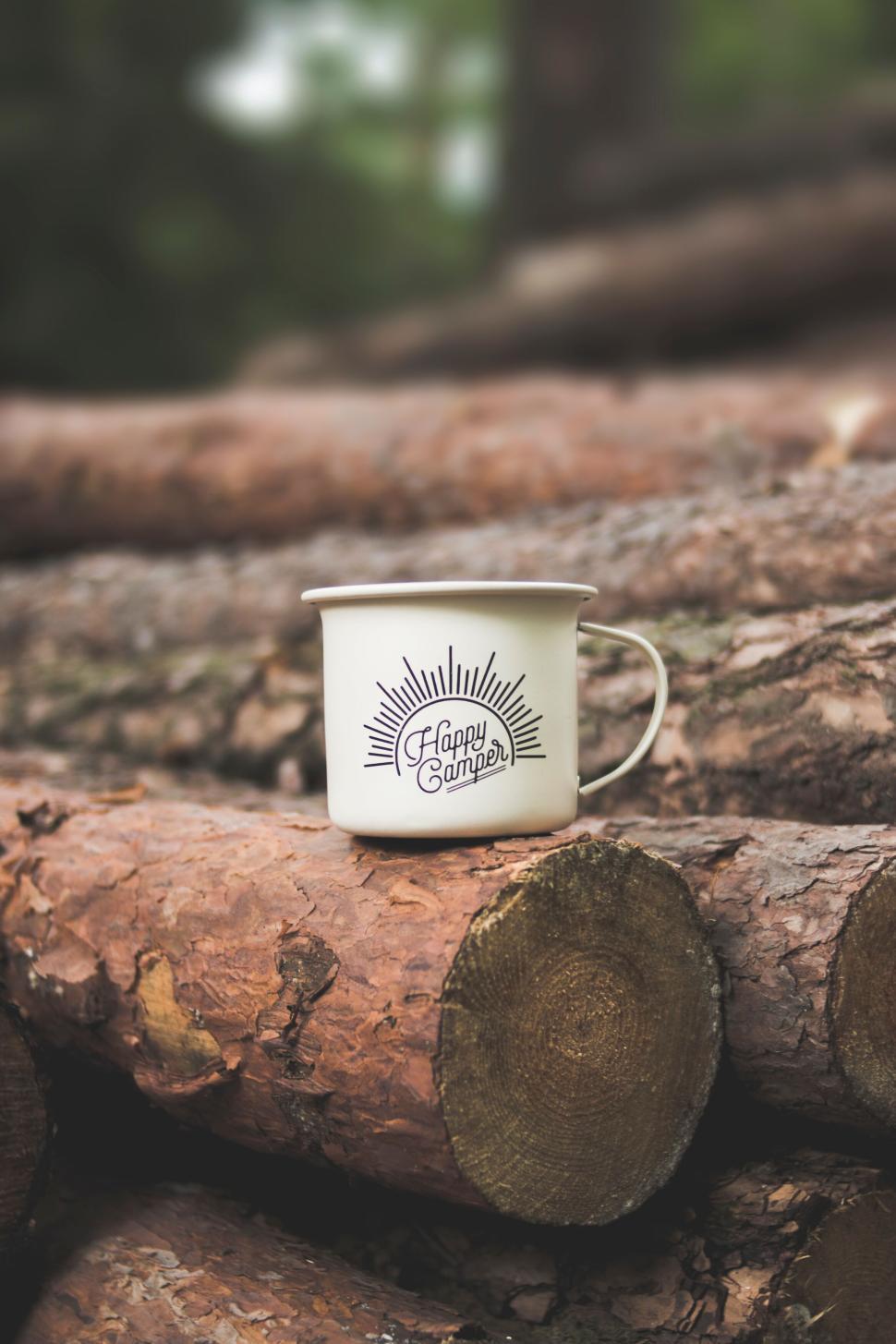 Free Image of White mug with Happy Camper logo placed on wooden logs 