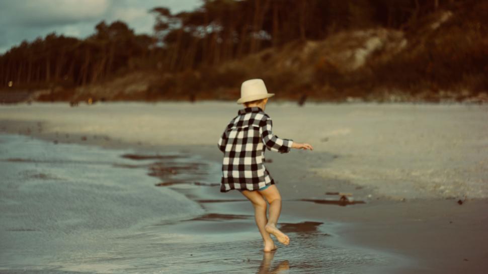 Free Image of Child playing on sandy beach wearing a hat and checkered shirt 