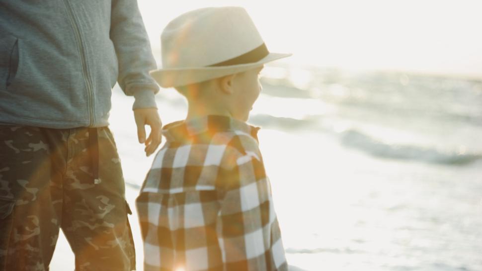 Free Image of Child wearing hat and plaid shirt standing by the sea 