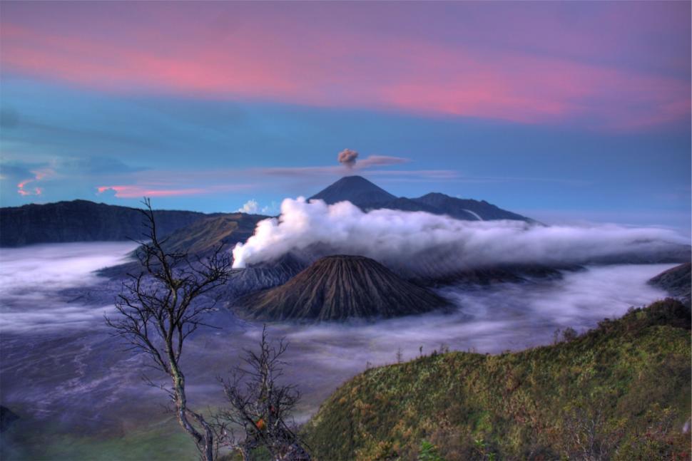 Free Image of Volcanic mountains under colorful sky with smoke rising. 