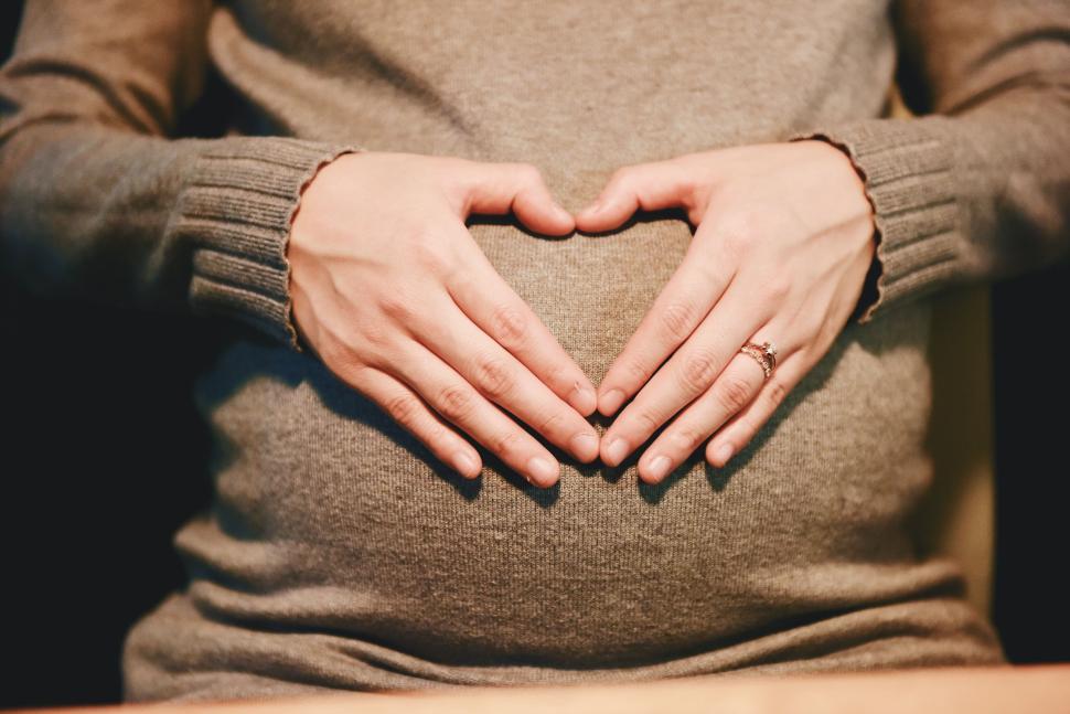 Free Image of Pregnant woman forming heart shape on belly with hands. 