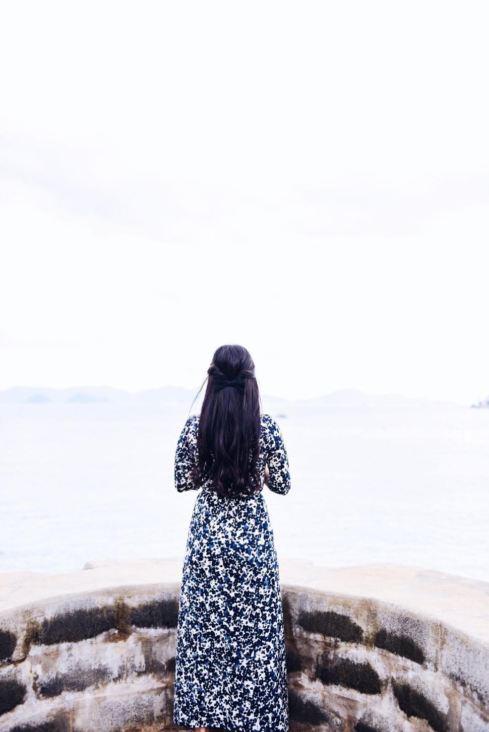 Free Image of Woman looking at serene ocean scene in a floral dress 