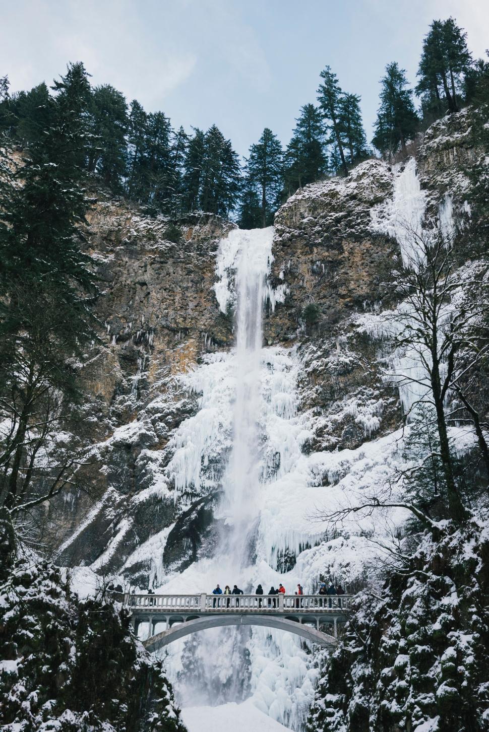 Free Image of Frozen waterfall with bridge and people in winter scene 