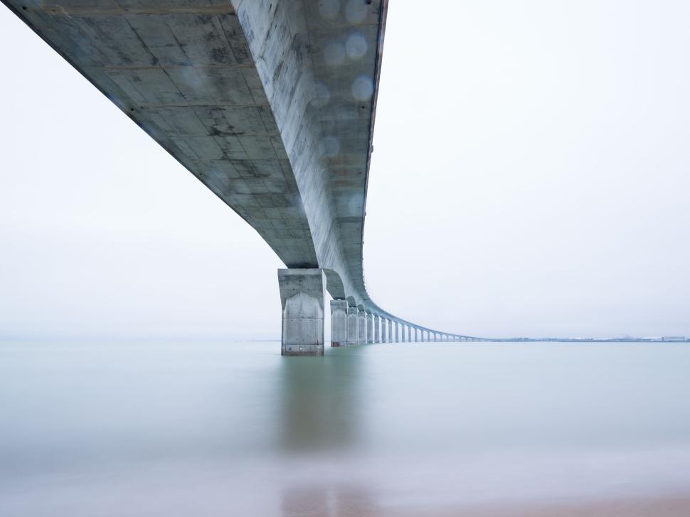 Free Image of Long bridge crossing over calm waters with distant horizon 