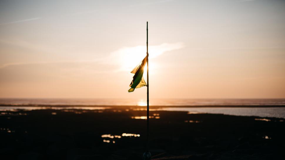 Free Image of Sunset beach with flag on pole in the golden hour 