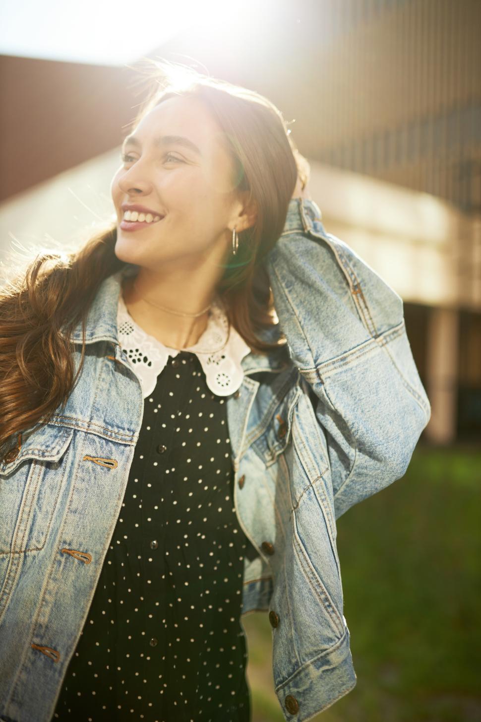 Free Image of Vertical picture of gorgeous youthful elegant romantic-looking girl in trendy clothes posing in sun light touching her hair gently, smiling, enjoying warm weather and walk down city streets 
