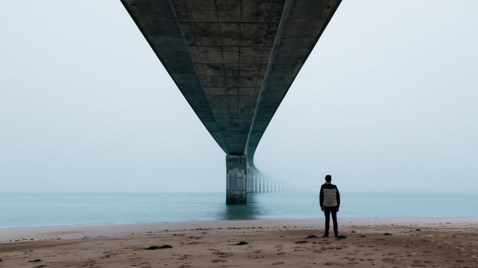 Free Image of Lone figure stands beneath vast, foggy bridge into horizon 
