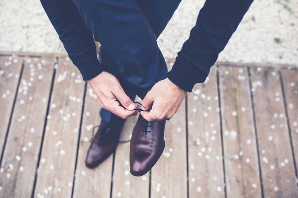 Free Image of A man tying the laces of his brown leather shoes 