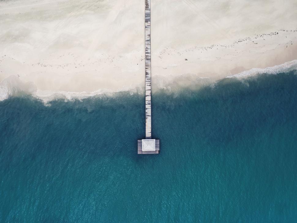 Free Image of Pier extending from sandy beach into turquoise ocean. 