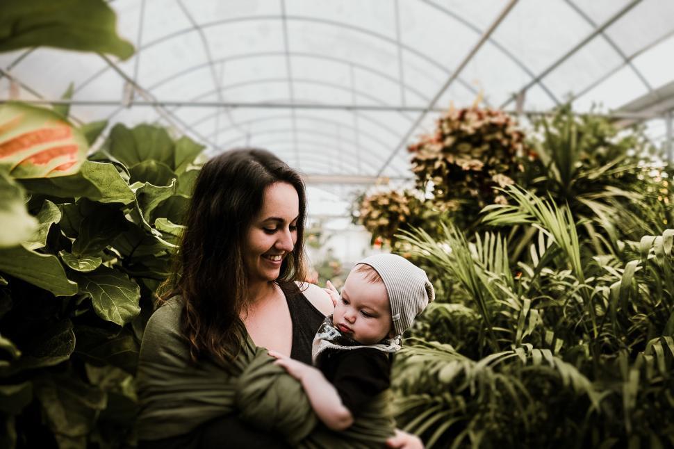 Free Image of Mother holding her baby in a lush greenhouse setting 