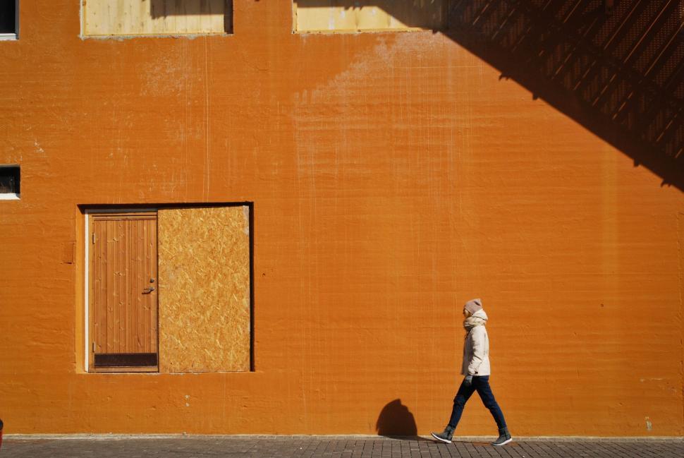 Free Image of Person walking beside brightly painted orange wall. 