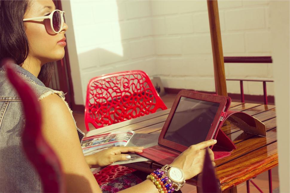 Free Image of Woman reading magazine while using tablet on terrace 