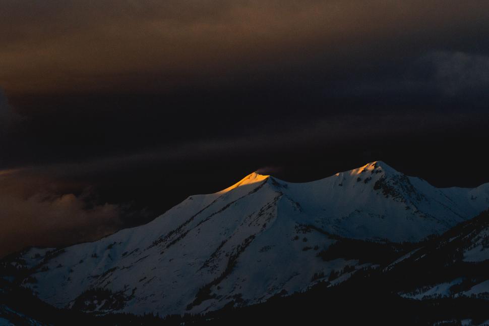 Free Image of Sunset glow on snow-capped mountain tops under dark sky 