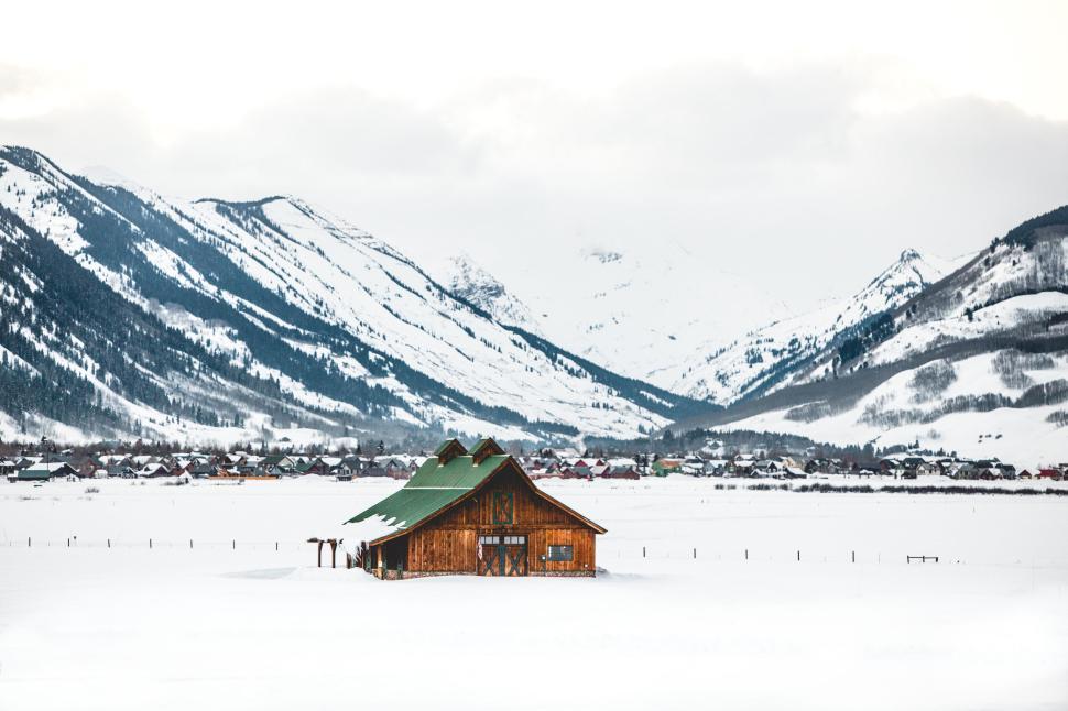Free Image of Snow-covered barn in mountain valley under cloudy sky. 