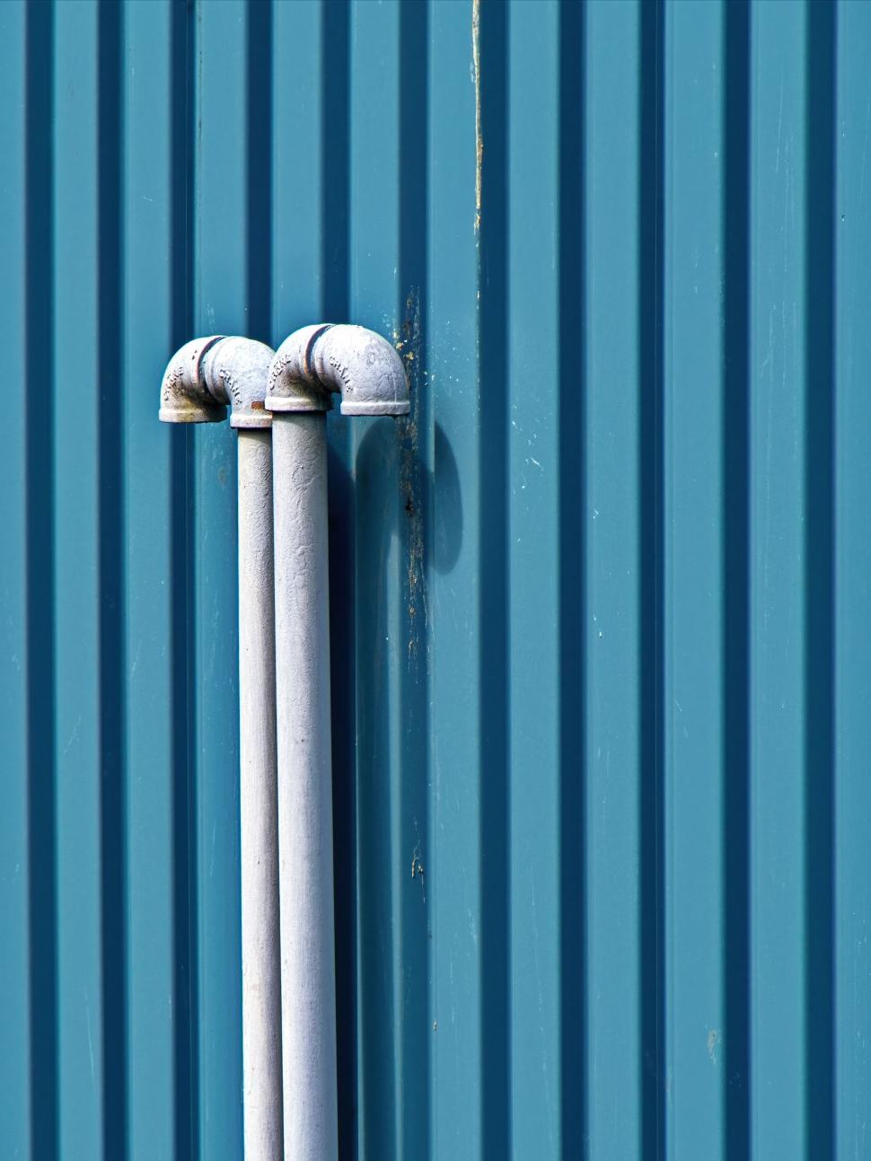 Free Image of Close-up of pipes on a blue corrugated metal wall. 