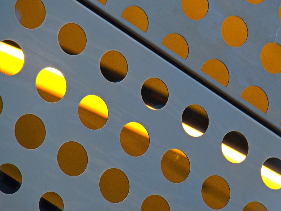 Free Image of Yellow lights seen through perforated metal sheets. 
