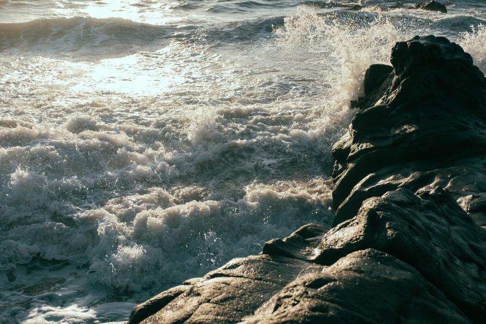 Free Image of Waves crashing against rocky shore in bright sunlight 