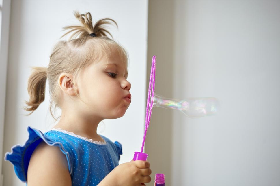 Free Image of Profile picture of adorable little girl of Caucasian appearance pouting her lips while blowing soap bubbles against white wall background with copy space for your text or advertising information 