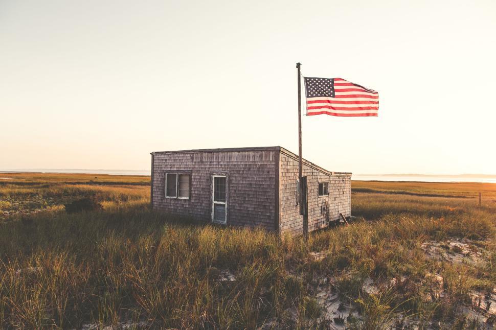Free Image of Small wooden house with American flag in field at dusk 