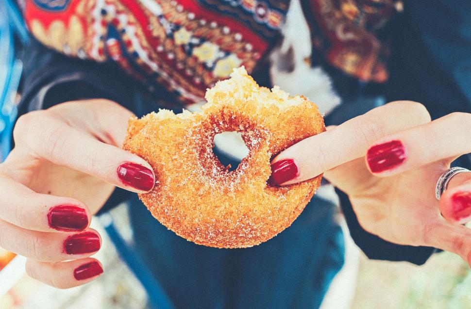 Free Image of Person with red nails enjoying a sugared donut. 