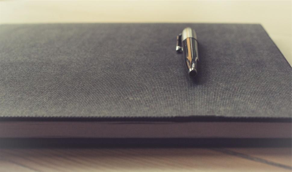 Free Image of Black notebook with silver pen on a wooden surface. 