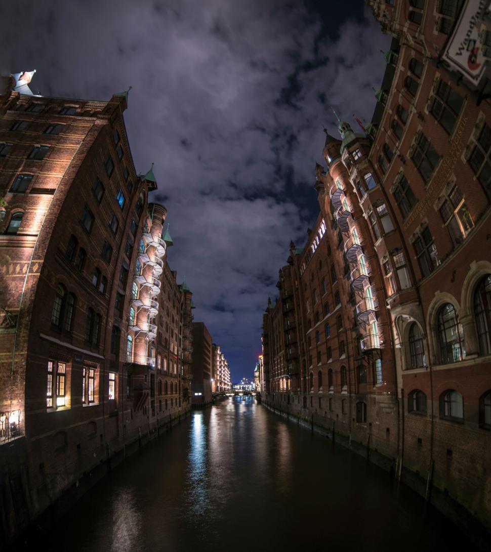 Free Image of Canal between tall buildings under a cloudy night sky. 