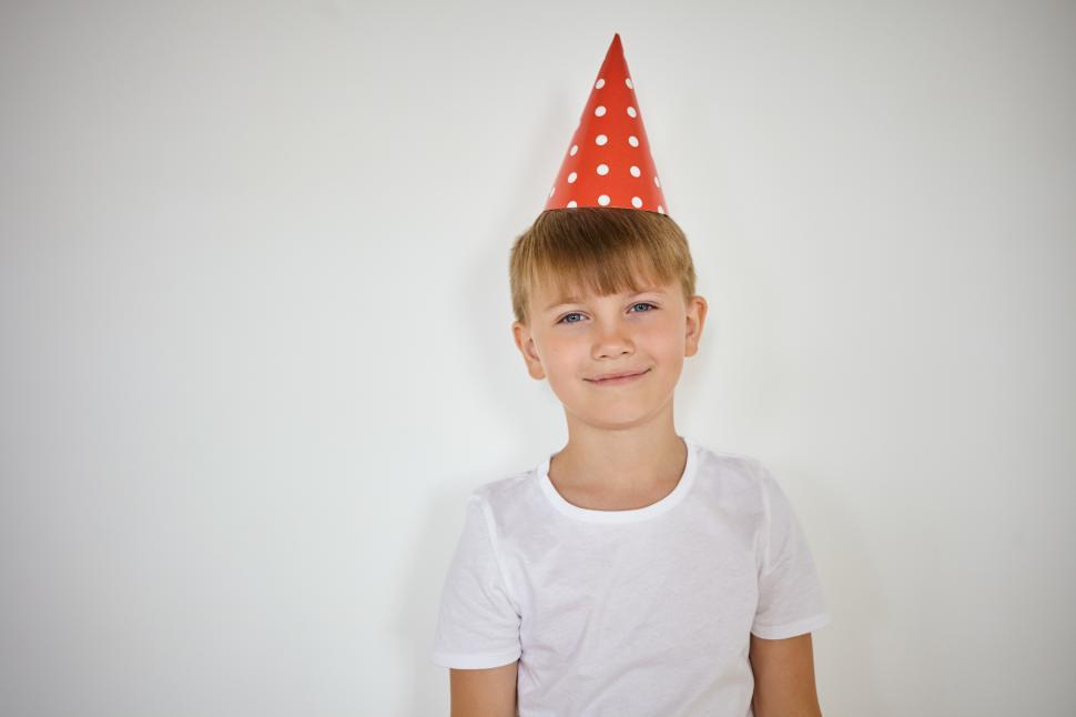 Free Image of Studio shot of handsome schoolboy with blue eyes and cute smile posing against white studio wall background with copy space for your text or advertising content, wearing red holiday cone hat 