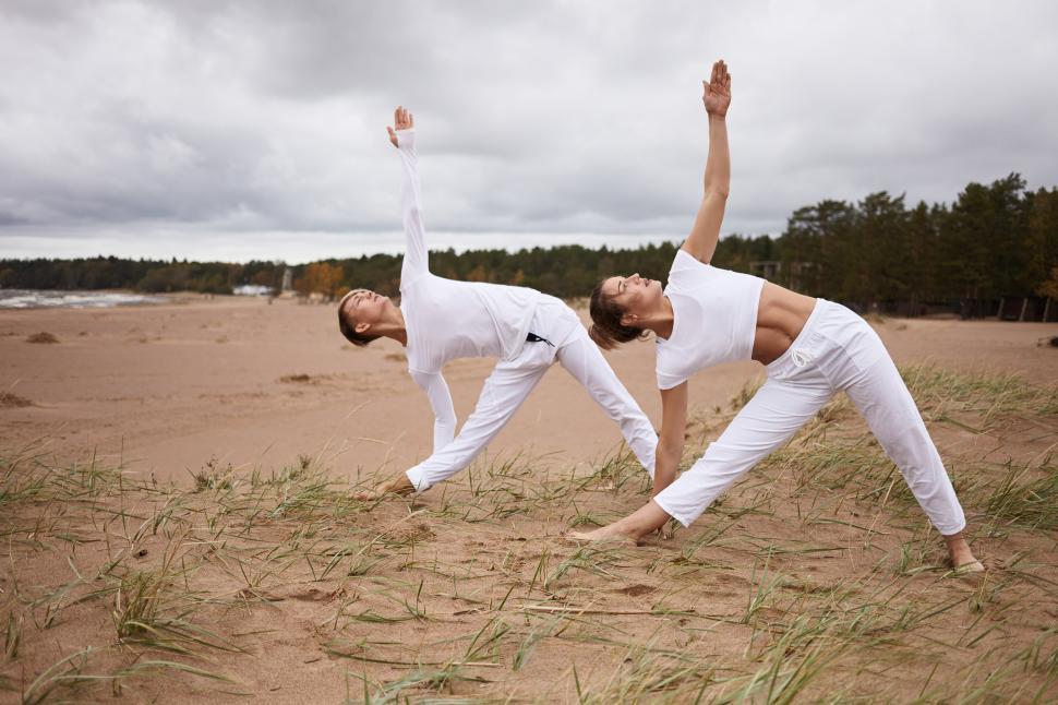 people-fitness-sport-friendship-family-and-lifestyle-concept.-professional-female-yoga-instructor-and-her-teenage-son-both-in-white-clothes-standing-barefooted-on-sand-doing-utthita-trikonasana.jpg