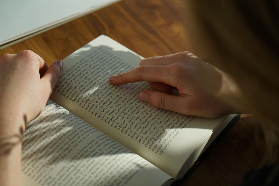 Free Image of Person reading a book with finger pointing at text. 