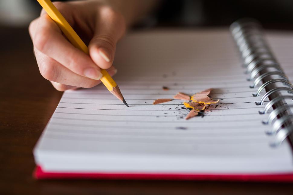Free Image of Hand writing in notebook with pencil and shavings. 