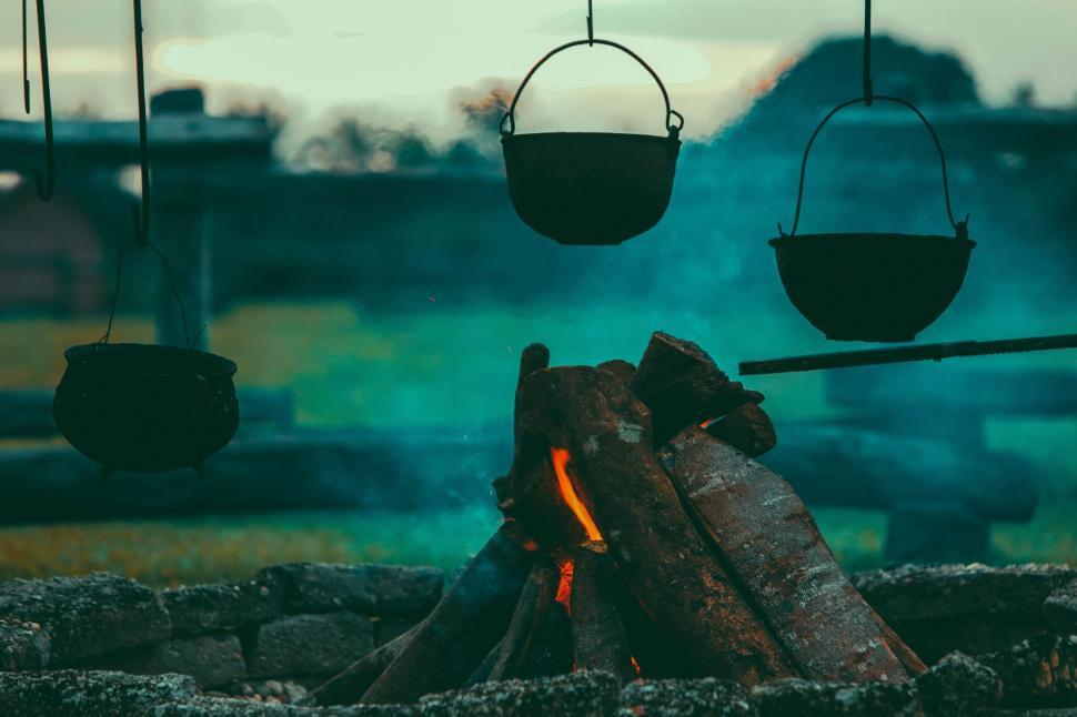 Free Image of Campfire with hanging pots under evening sky in rustic setting 