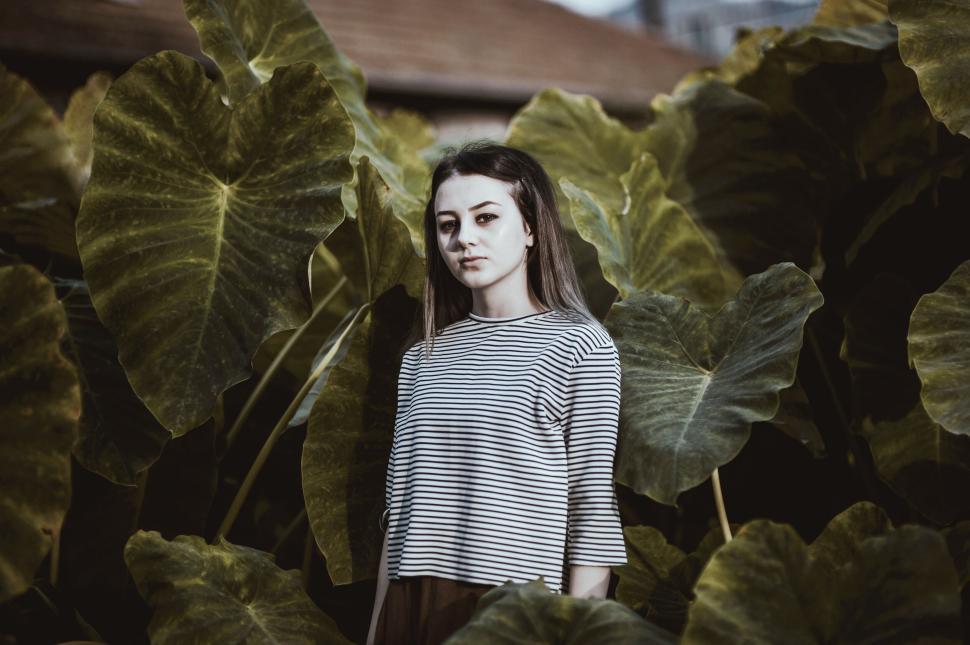 Free Image of Woman in striped shirt standing among large green leaves. 