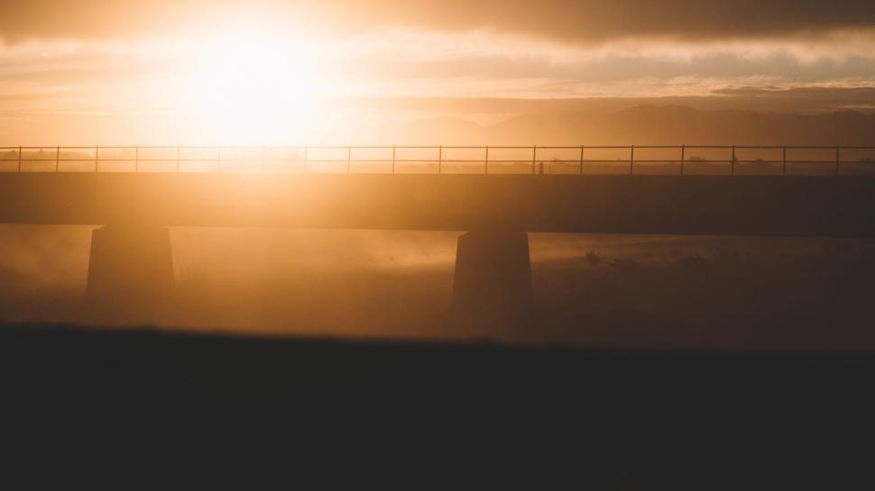 Free Image of Sunset casting golden light over a bridge in the distance 