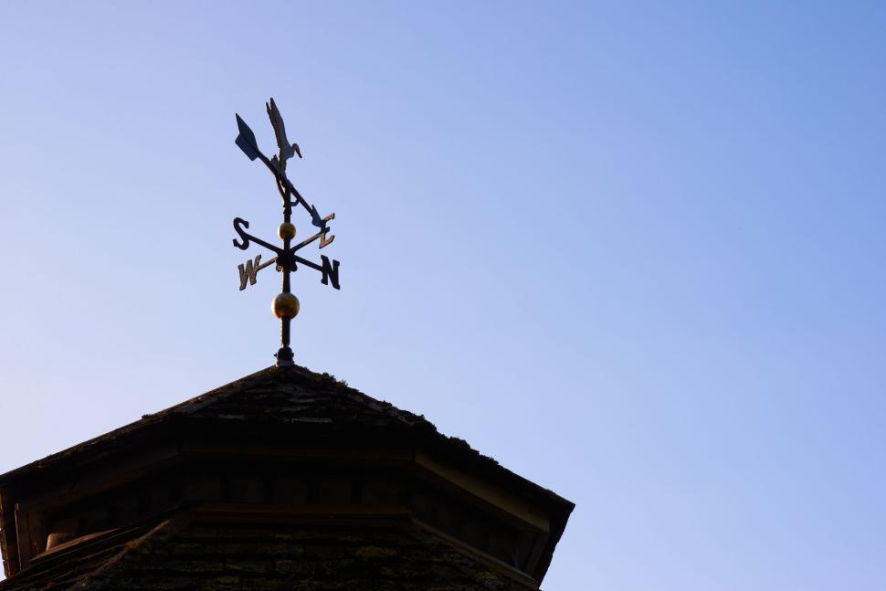 Free Image of Weather vane on top of a roof under a clear blue sky 
