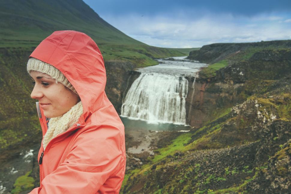 Free Image of Woman in orange jacket in front of scenic waterfall view 