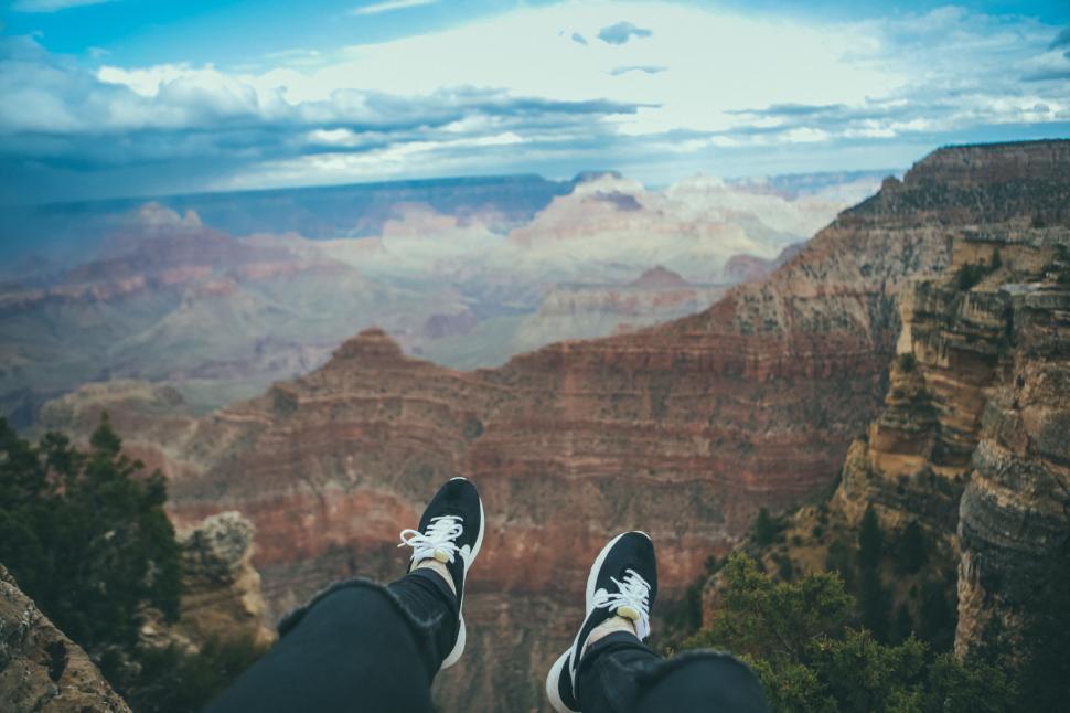 Free Image of Person sitting and dangling legs over vast canyon 