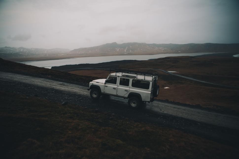 Free Image of Off-road vehicle driving on gravel path by a lake 
