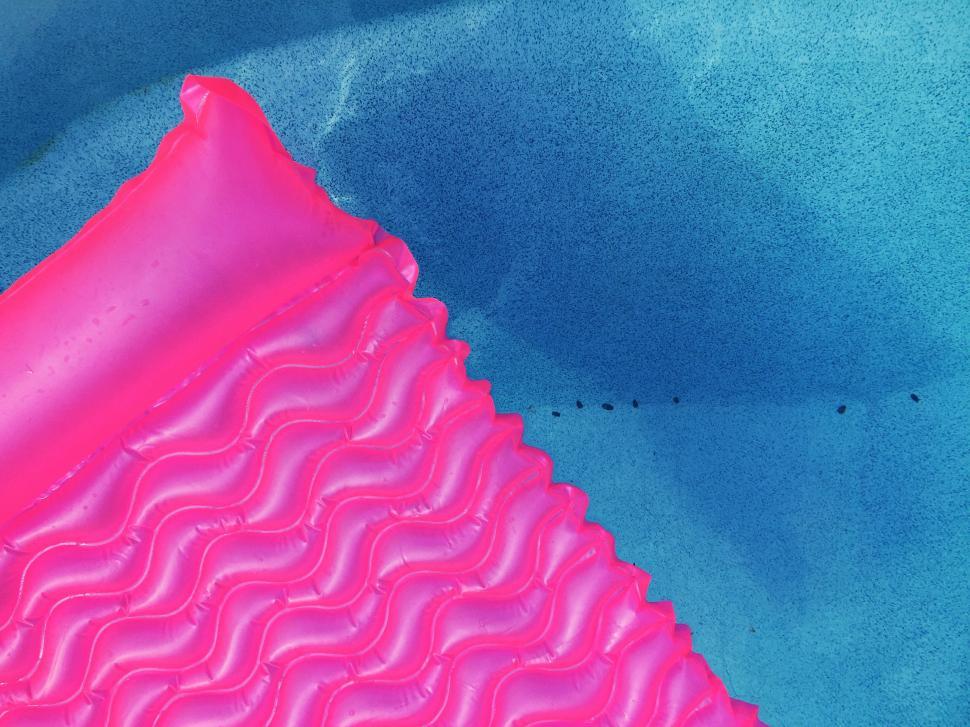 Free Image of Pink inflatable mattress floating in a clear blue pool 