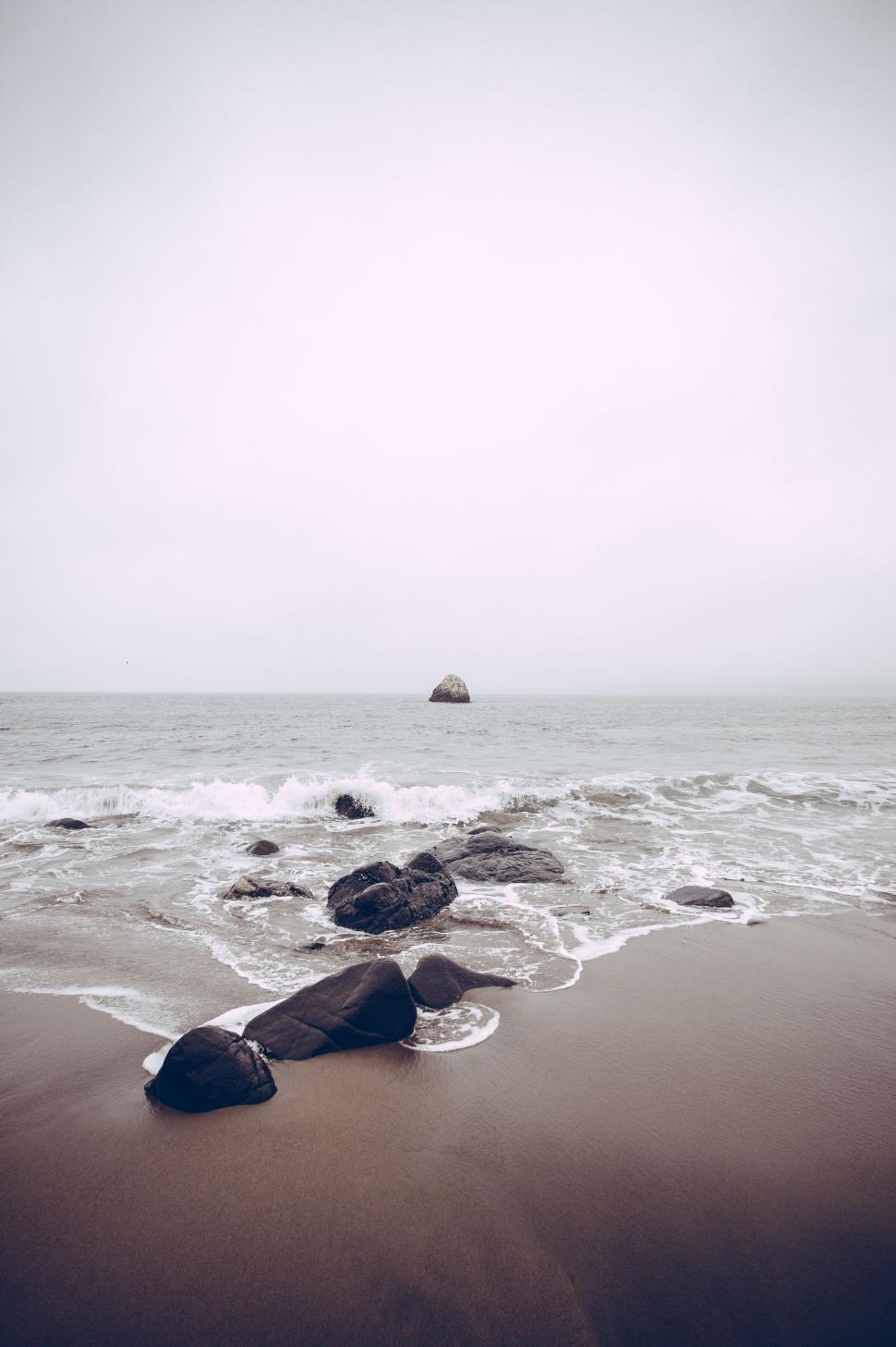 Free Image of Waves crashing on beach with solitary rock ahead in mist 