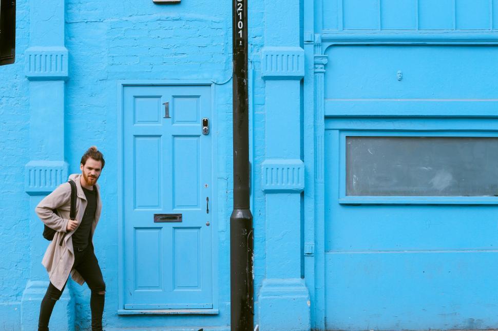 Free Image of Man standing by blue door and wall in stylish outdoor pose 