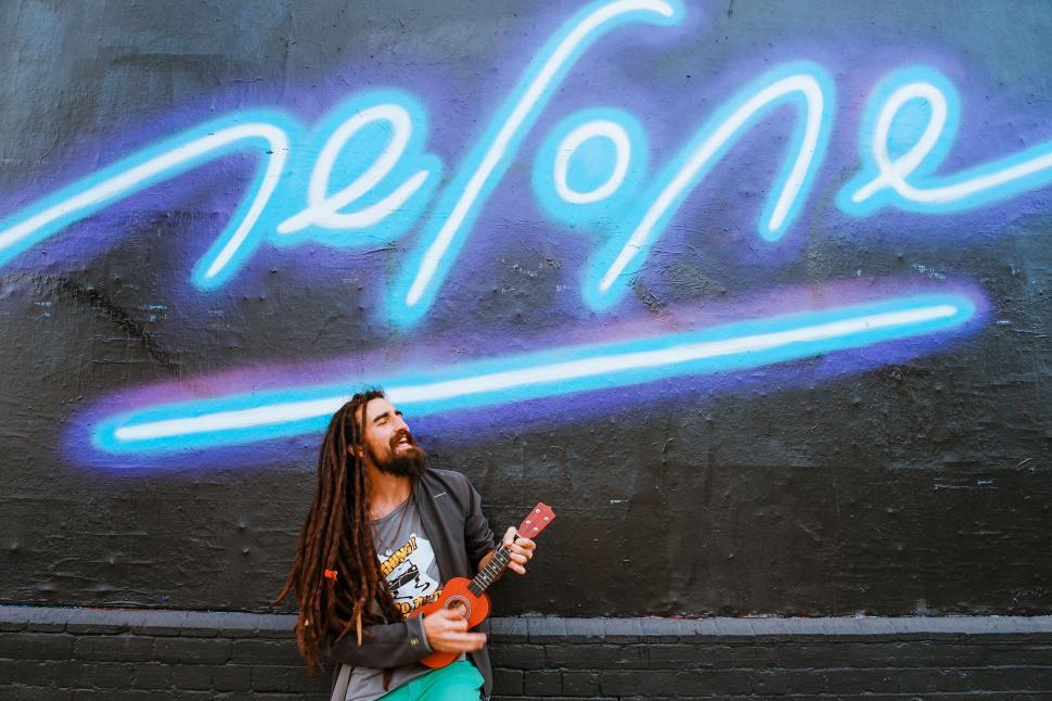 Free Image of Musician playing ukulele in front of neon sign. 