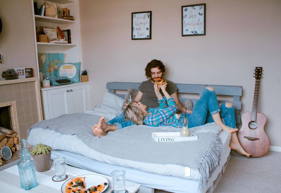 Free Image of Couple enjoying pizza together in cozy bedroom setting 
