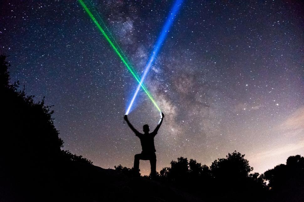 Free Image of Man at night under starry sky holding colorful light beams 