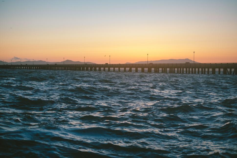Free Image of Sunset pier extending into rough ocean waters and waves. 